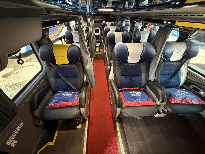 Interior do ônibus Transmar com poltronas reclináveis e corredor com carpete vermelho